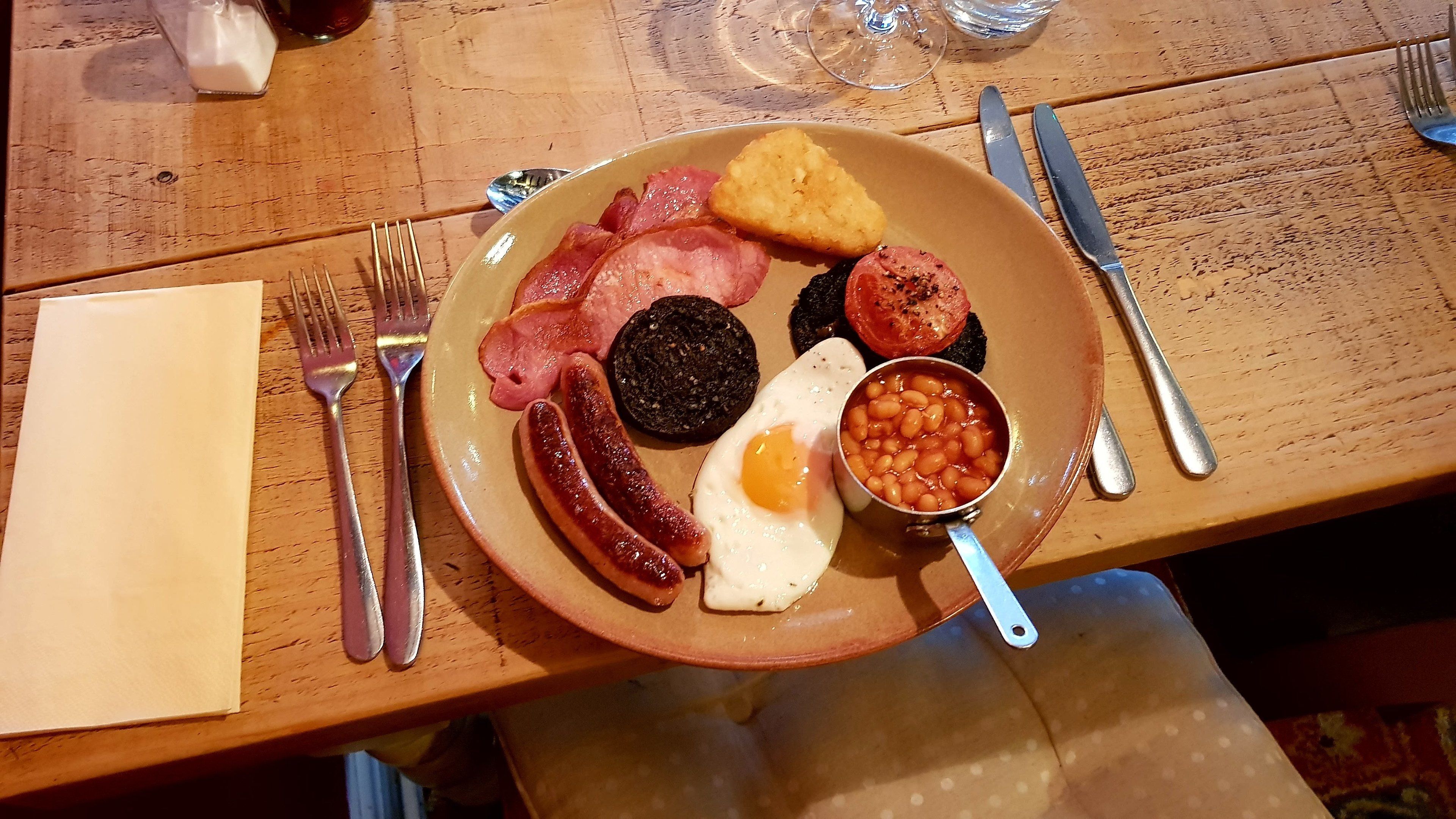 En morgenmadstallerken med pølser, æg, bønner og ristet brød på et træbord.