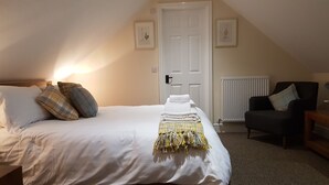 Une chambre à coucher avec un lit, des oreillers, une chaise, un radiateur et des tableaux encadrés accrochés au mur.