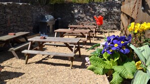 Une terrasse extérieure avec des tables et des bancs en bois, entourée d’un mur de pierre et recouverte de gravier.