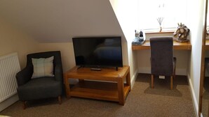 Un salon avec un téléviseur posé sur un meuble en bois, un fauteuil sombre et un bureau avec une chaise.
