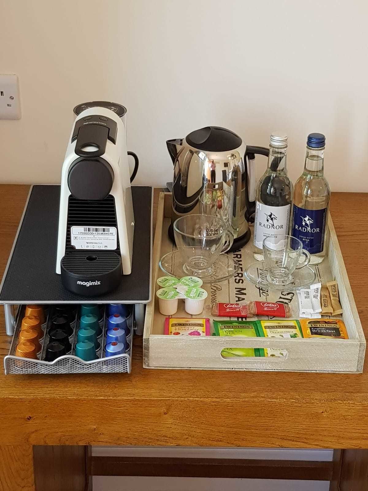 A coffee maker, a kettle, two bottles of Radnor, glasses, and a tray with snacks and condiments.