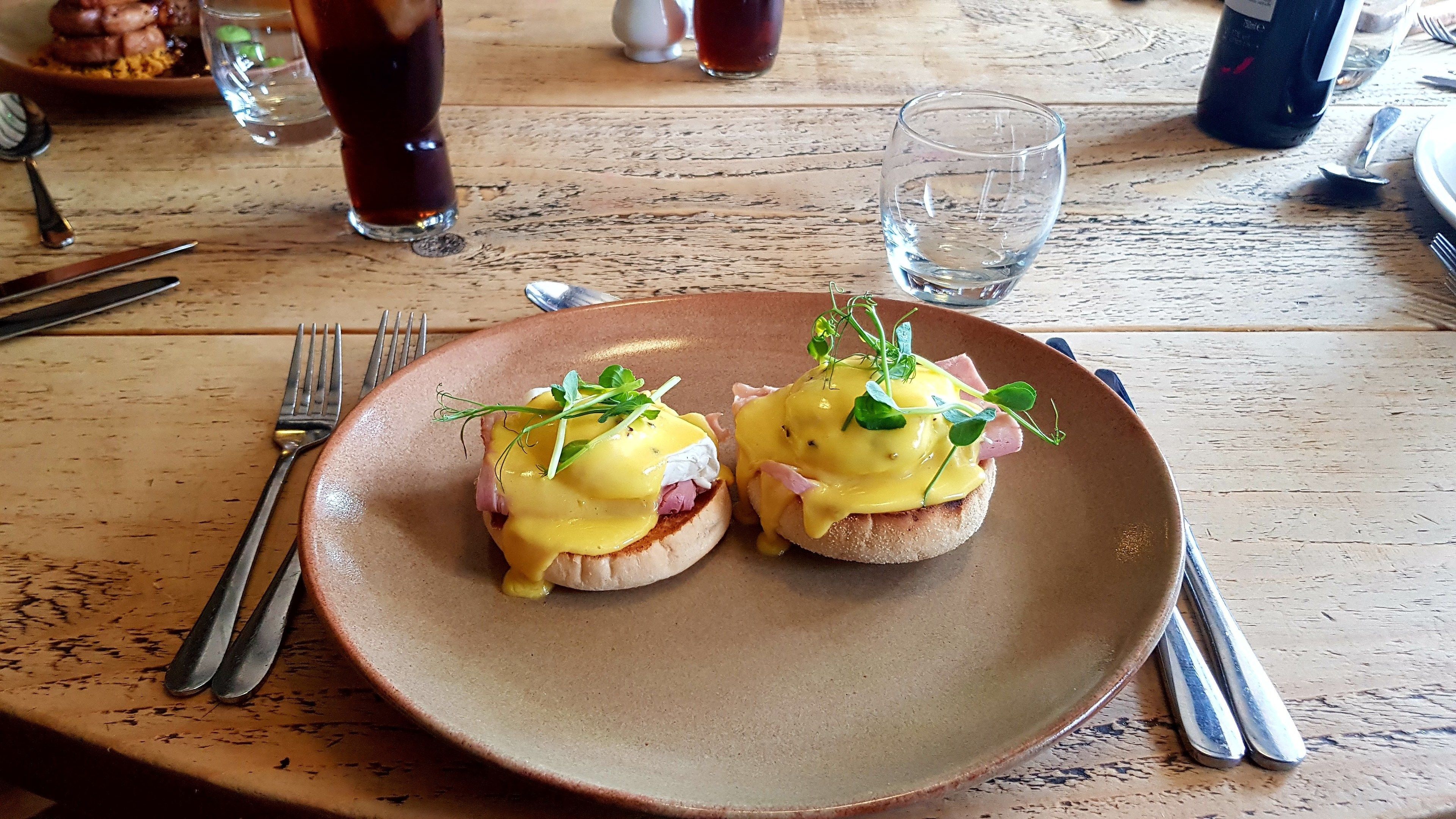 Une assiette avec deux sandwichs aux œufs Bénédicte, posée sur une table en bois.