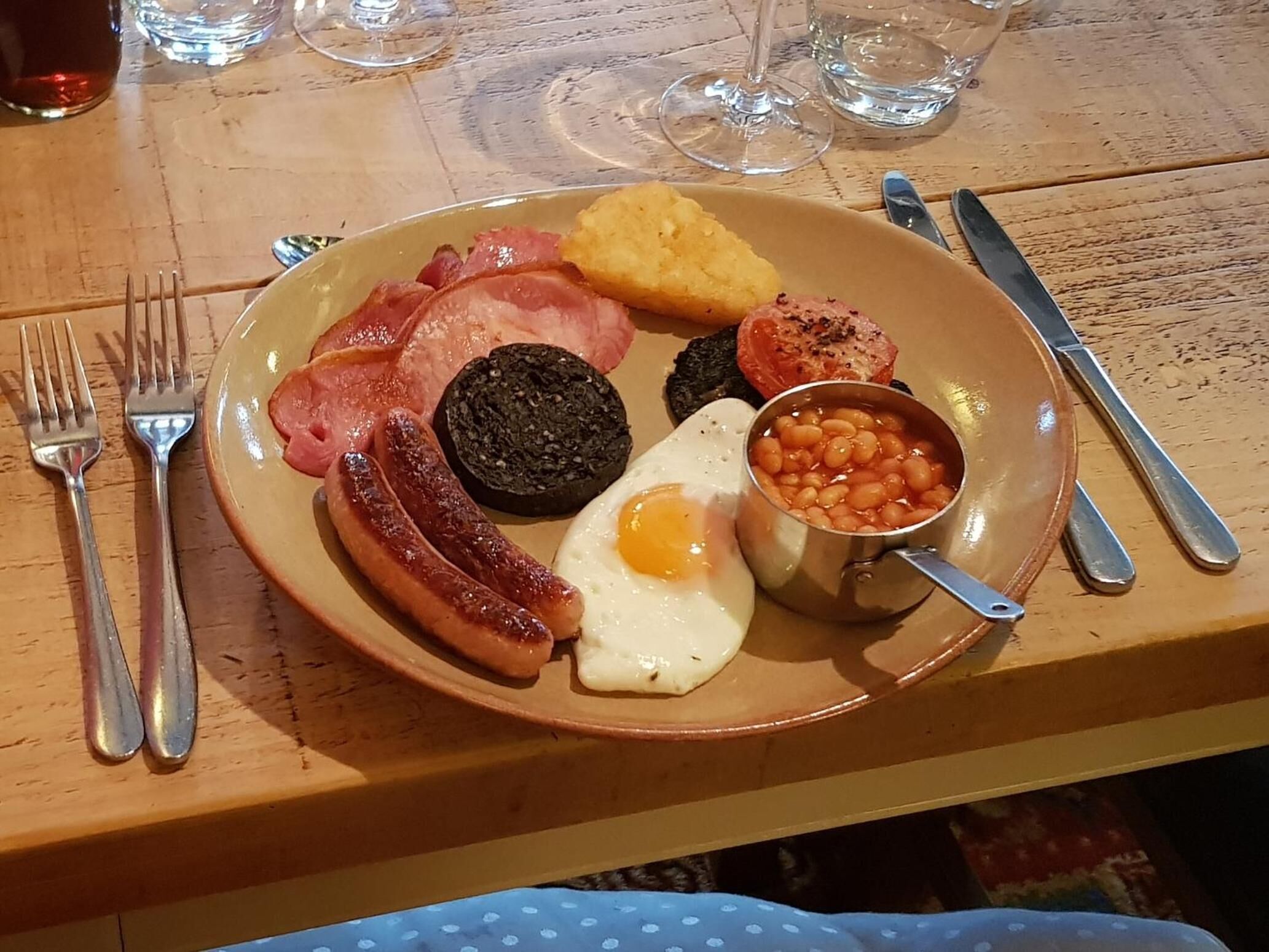 Un plato de comida para el desayuno con salchichas, tocino, huevos, frijoles y morcilla.