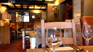 L’intérieur d’un restaurant, avec des meubles en bois, une moquette rouge à motifs et une table dressée pour deux personnes, avec des verres à vin et des couverts.