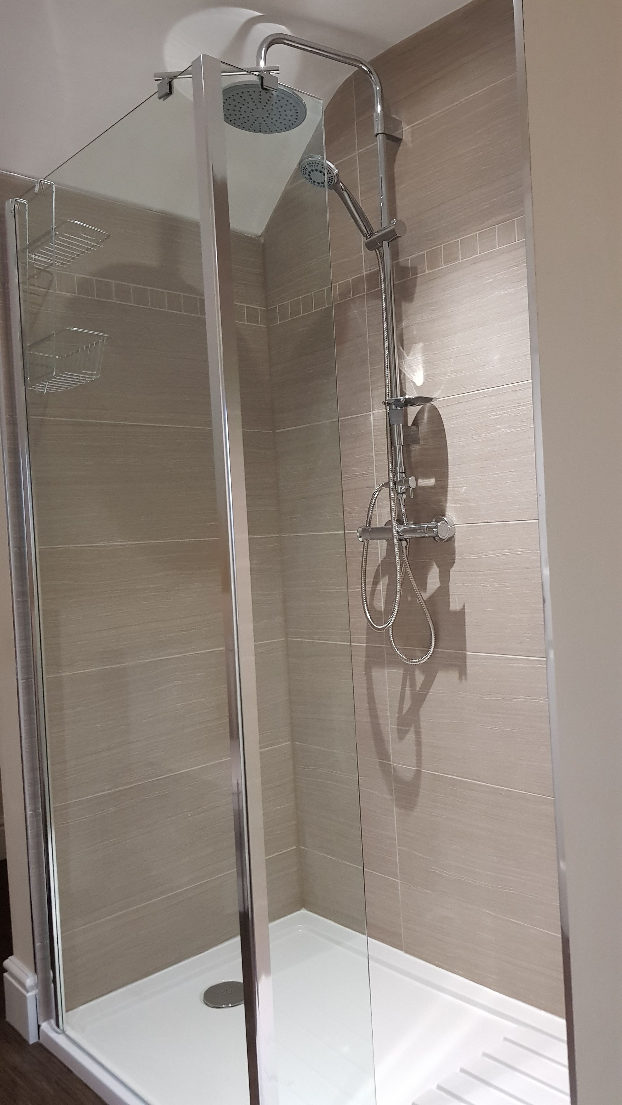A glass-enclosed shower stall with a handheld showerhead and a handheld shower attachment.