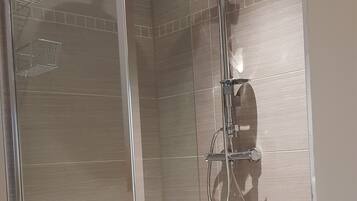 A glass-enclosed shower stall with a handheld showerhead and a handheld shower attachment.