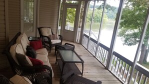 Eine überdachte Veranda mit Korbmöbeln, einem Glastisch und Blick auf einen See.