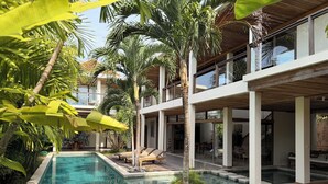 A modern pool area with clear water, surrounded by palm trees and lounge chairs.