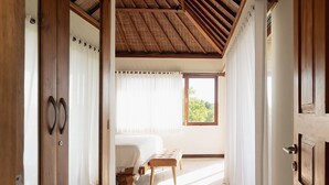 A room with a wooden ceiling, a bed, a bench, and a window with curtains.