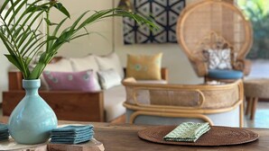 A wooden dining table with woven placemats and a blue vase with green plants.