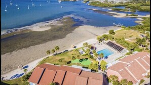 Vista aérea de una zona costera con playa, piscina y un puerto deportivo con barcos.
