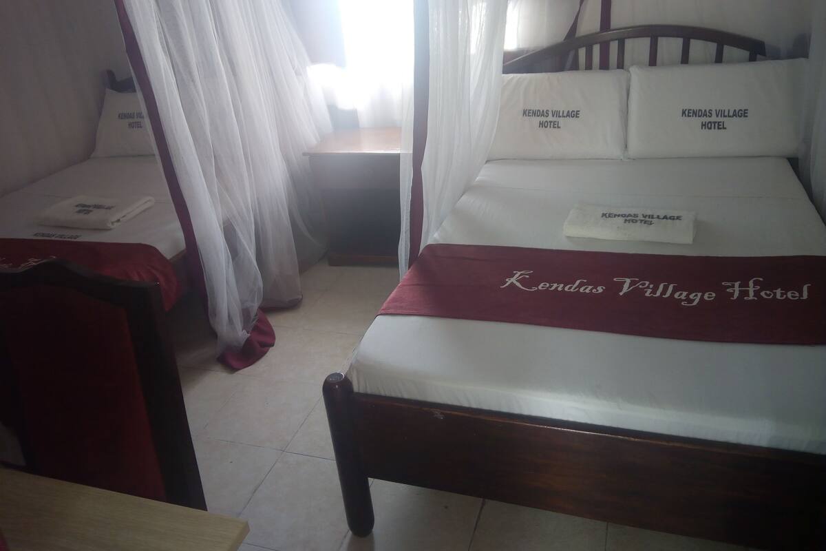 A room with a bed, a bedside table, and a chair. There are two pillows with the hotel name on them.