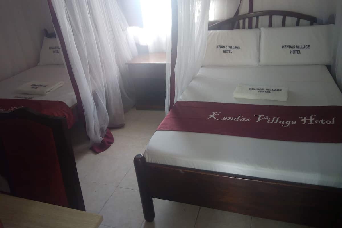 A hotel room with a bed, a wooden headboard, a red throw blanket, and a canopy bed with a white sheet.