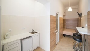 A compact kitchen with a sink, cabinets, and a small refrigerator. There is a bar stool and a bench in the adjacent area. - Smart Apartment Kulisha 29a (Lviv)