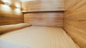 Quarto com paredes de madeira, cama com colchão texturizado e iluminação fixada na parede.