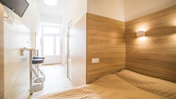 A modern bedroom with a wooden headboard, a bed with a beige quilt, a small stool, and a TV mounted on the wall. - Smart Apartment Kulisha 29a (Lviv)