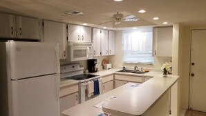 A modern kitchen with white cabinetry, a refrigerator, a microwave, an oven, a sink, and a ceiling fan. - The entrance on Siesta Key (Siesta Key)