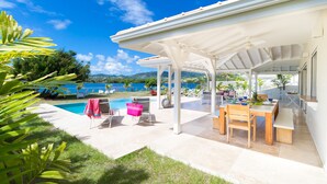 A covered outdoor area with a pool, lounge chairs, and a dining table. - Céladon (Le François)