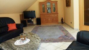 A living room with a black leather sofa, a glass coffee table with a decorative item, a wooden cabinet, and a television. - "Nice living in Mainz" Apartment Gisela & Jürgen Will  (Gonsenheim)