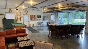 A spacious indoor area with a pool table, a bar area with stools, and a seating area with a sofa and chairs. - Blue Bear Hideout the ultimate set up for large groups and get togethers! (Kalkaska)