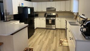 A modern kitchen with white cabinets, a black refrigerator, stainless steel appliances, and a wooden floor. - Blue Bear Hideout the ultimate set up for large groups and get togethers! (Kalkaska)