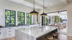 Une cuisine spacieuse dotée d’un grand îlot en marbre, d’un éclairage suspendu et offrant une vue sur l’extérieur.