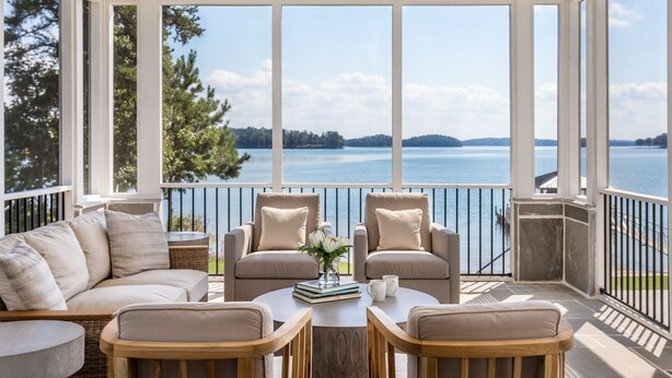 Un balcon ensoleillé avec vue sur un lac, aménagé avec un canapé, des fauteuils et une table.