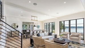Un vaste salon doté d’une grande fenêtre donnant sur le lac, un coin salon confortable avec un canapé et des fauteuils, et un escalier muni d’une rampe.
