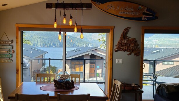 Un espace repas doté d’une grande fenêtre donnant sur un paysage montagneux, d’une table en bois et de plusieurs luminaires suspendus.
