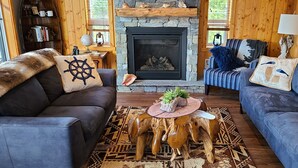 Un intérieur de chalet chaleureux avec une cheminée en pierre, des canapés en cuir et une table basse en bois rustique.