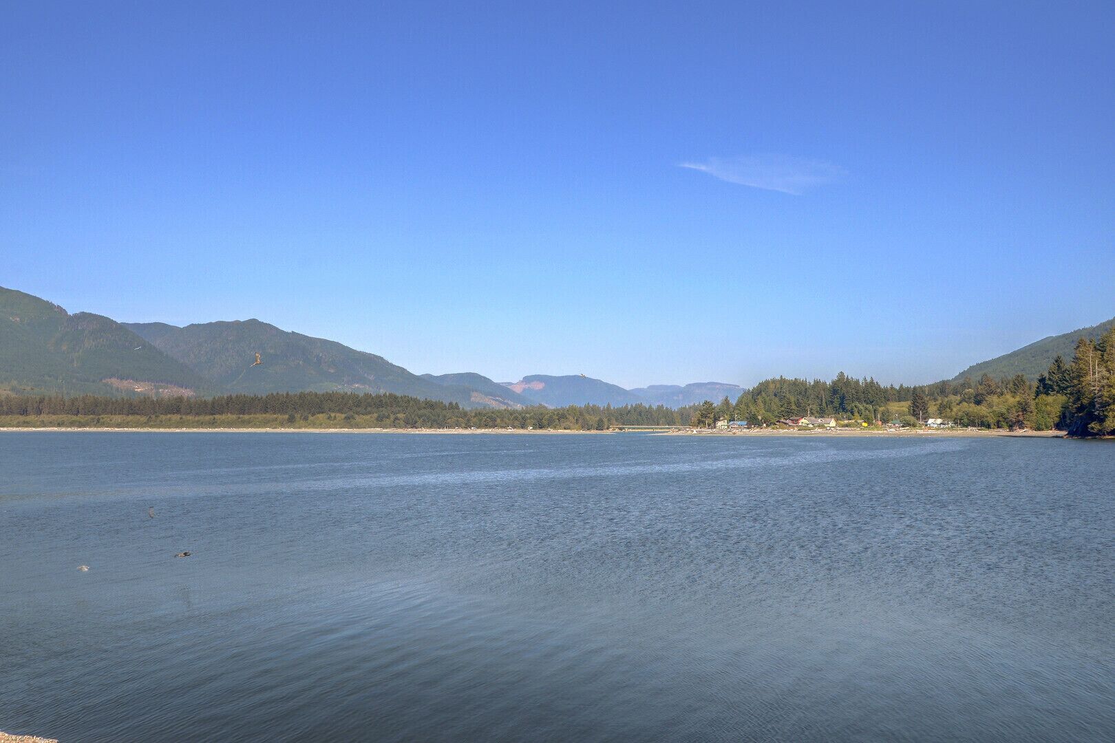 Un lago tranquilo con montañas al fondo y un cielo despejado.