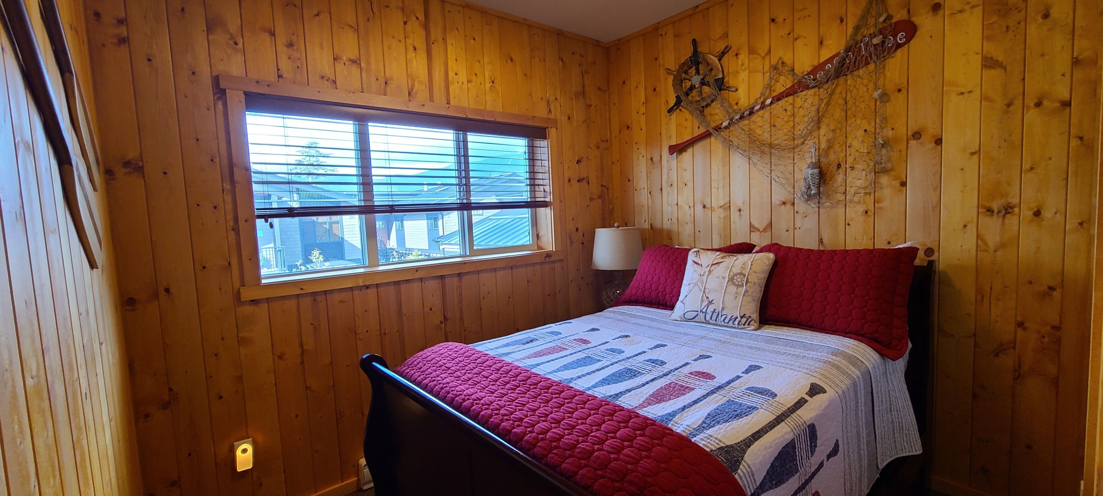 Ein Zimmer mit Holzwandverkleidung, einem Bett, einem Fenster und einem an der Wand befestigten Schiffsschwengel.