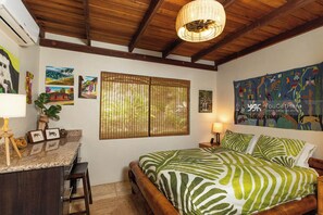Une chambre à coucher comprenant un lit, un bureau, des chaises, une fenêtre avec des stores, un luminaire suspendu et des œuvres d’art murales.