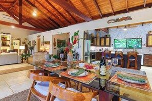 A spacious dining area with a glass table, wooden chairs, and a view of the kitchen.