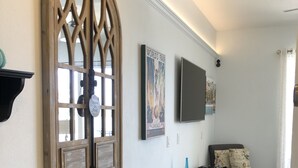 Een moderne woonkamer met een groot rondboogvenster, een flatscreen televisie aan de wand, een zwarte mediakast en een grijze bank.