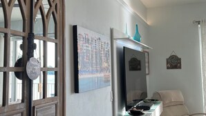 Een moderne woonkamer met een groot raam, een flatscreen-tv, een massagestoel en een bureau met een computer.