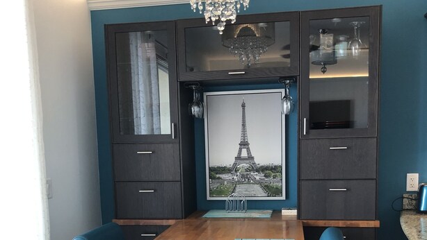 Een eetruimte met een houten tafel, blauwe stoelen, een kroonluchter en een lijst met een afbeelding van de Eiffeltoren.