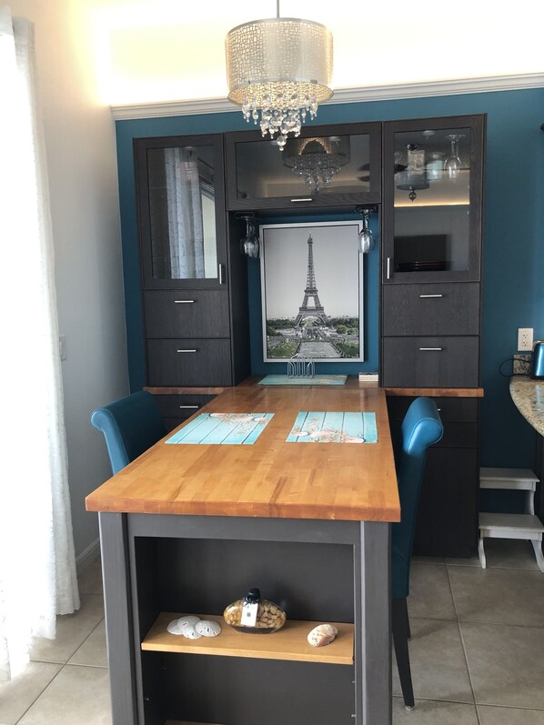 Un coin repas avec une table en bois, des chaises bleues, un lustre et un tableau encadré représentant la Tour Eiffel.