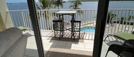 Un balcon donnant sur une piscine et des palmiers, une table avec des chaises et un canapé.