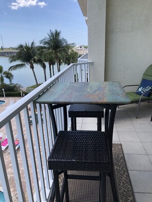 Un balcon avec une table et des chaises, donnant sur une étendue d’eau et des palmiers.