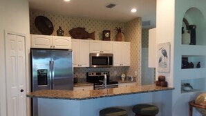A kitchen with white cabinets, stainless steel appliances, and a granite countertop. There are two stools at the island.