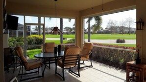 A sunlit patio with a table and chairs, a ceiling fan, and a view of a golf course.