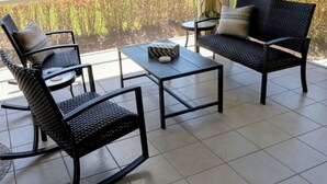A covered patio with two rocking chairs, a small table, and a view of a golf course.