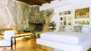 A bedroom with a stone wall, wooden floor, a bed with white bedding, a bench, and artwork on the wall. - VILLA SHAH a place to listen to the sea in Amalfi Coast (Conca dei Marini)