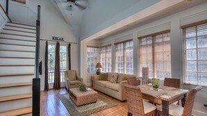 Uma sala de estar espaçosa com escada, sofá, mesa de jantar com cadeiras e janelas amplas com persianas.