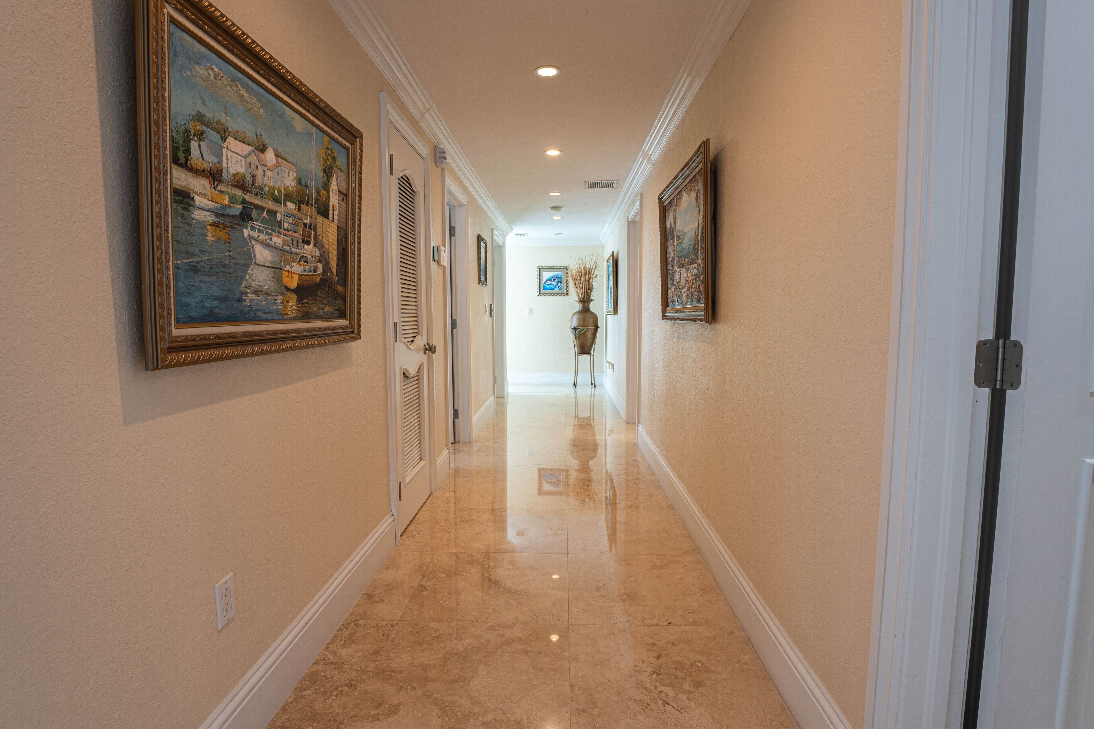 A hallway with a polished floor, framed artwork on the walls, and a door at the end.