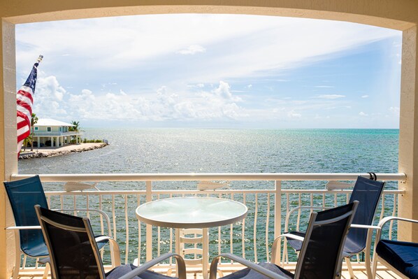 A balcony with a view of the sea, a flag, and a table with chairs.