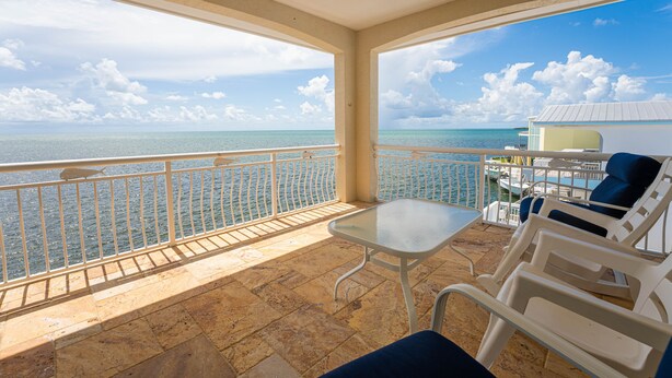 A balcony with a view of the sea, a table, and lounge chairs. - Luxury Home King Beds Ocean View 5 Min To Sandbar, Best Keys Experience! (Tavernier)