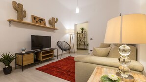 Een moderne woonkamer met een televisie, bank, rood vloerkleed en een decoratieve cactus.