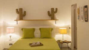 Hotelkamer met een bed, twee groene kussens, een dienblad met theeservies, een cactussieraad en een wandplank.